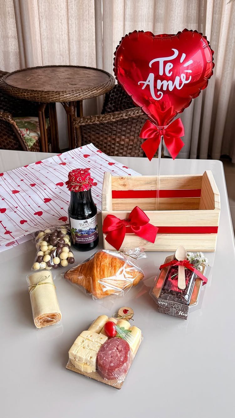 Wooden gift crate with red ribbon, heart balloon, charcuterie, and assorted gourmet treats.