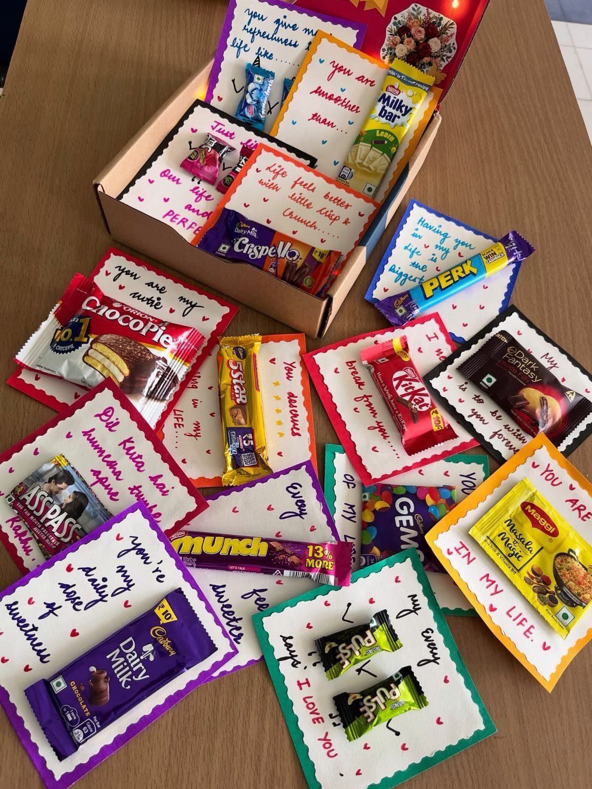 Assorted chocolate bars and candies with handwritten romantic notes in a gift box.