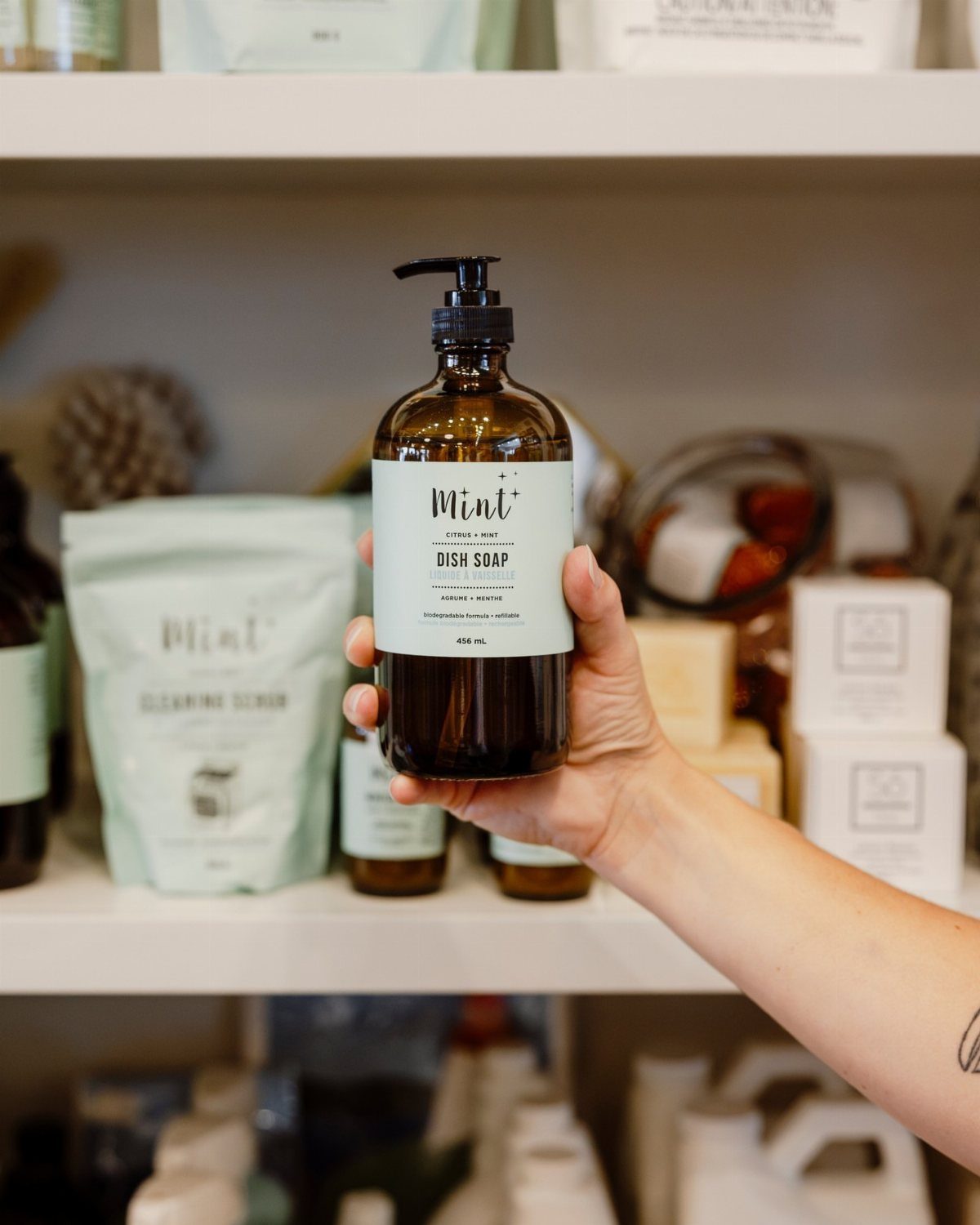 Hand holding a brown glass bottle of dish soap on a store shelf.