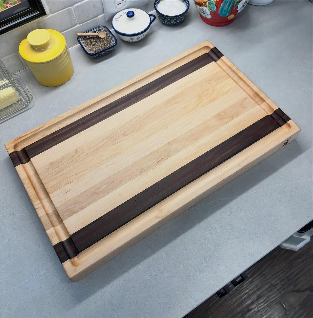 Wooden cutting board with dark walnut stripes and juice grooves on a grey countertop