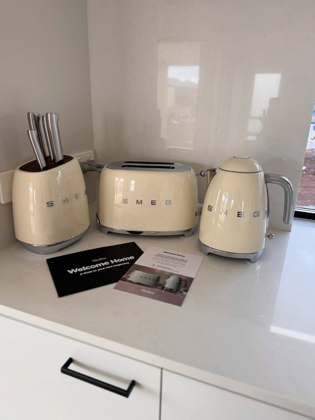 Cream Smeg kitchen appliances including a toaster, kettle, and knife block on white counter.