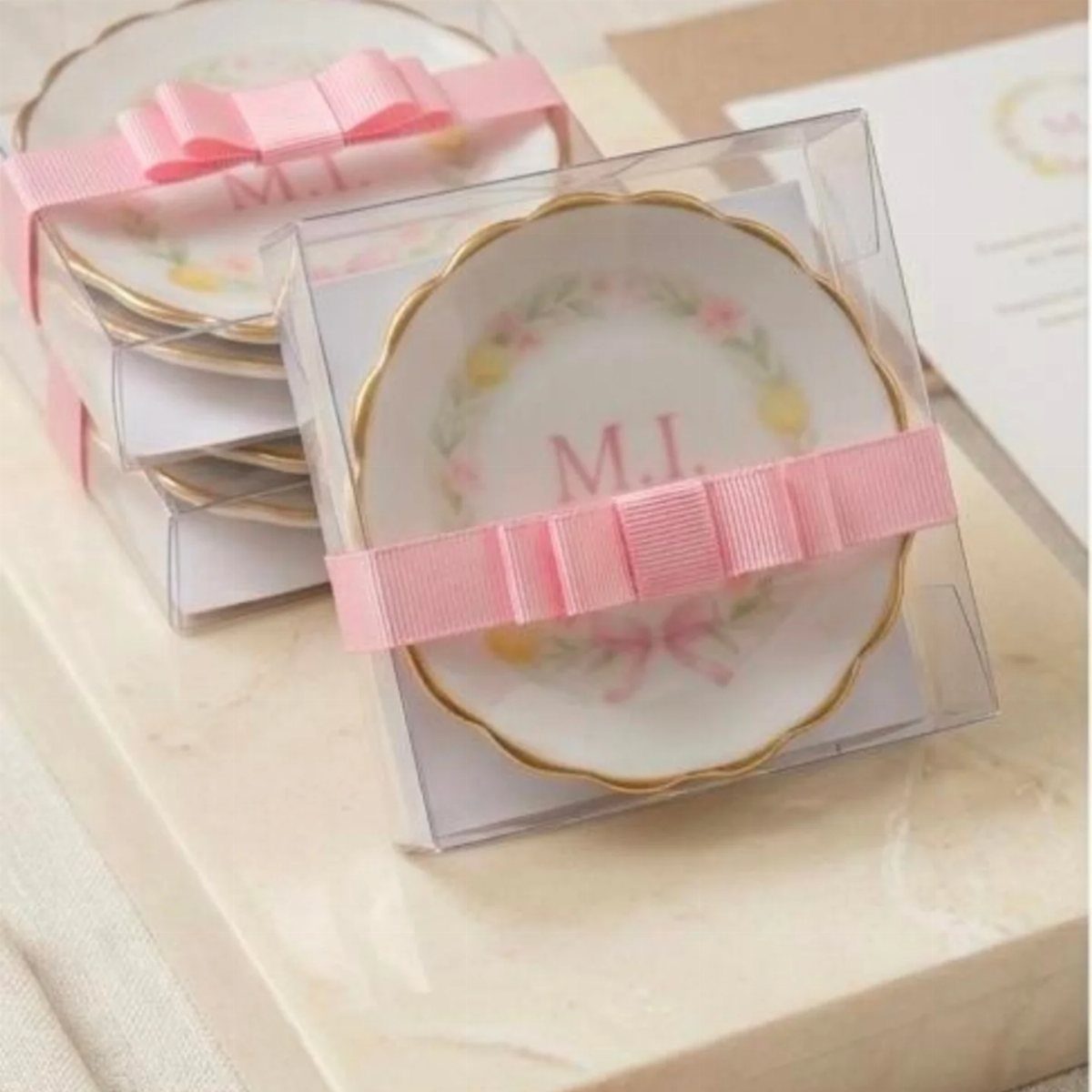 Monogrammed white ceramic trinket dishes with pink ribbons in clear gift boxes.