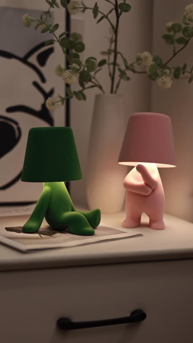 Two small humanoid lamps in green and pink on a white dresser.