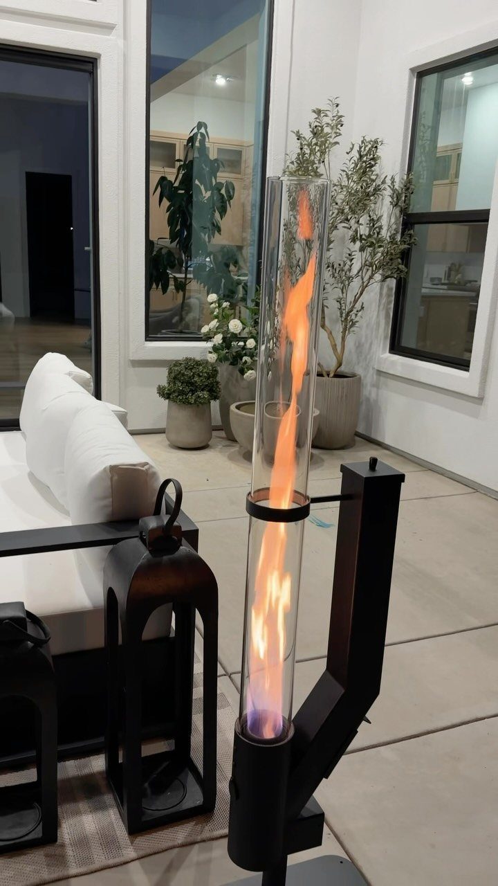 Cylindrical glass fire pit with orange flames on a modern concrete patio