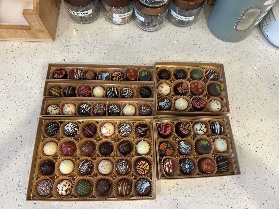 Assorted gourmet chocolate truffles in four open brown cardboard gift boxes.
