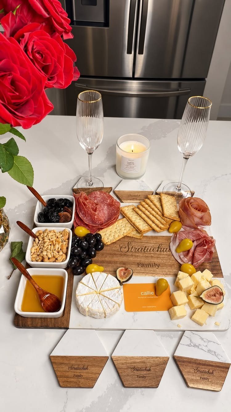 Cheese board with meats, cheeses, and crackers next to champagne glasses and roses.