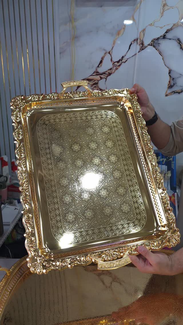 Ornate gold metal tray with intricate patterns held by two hands.