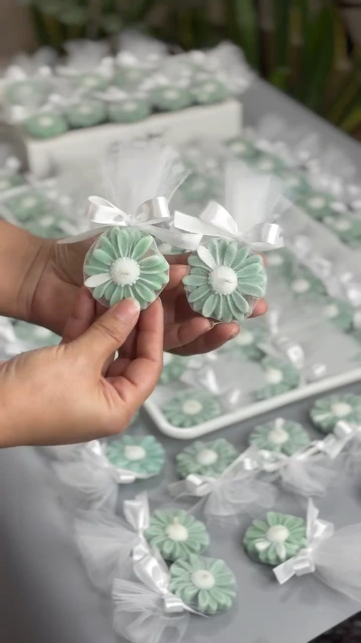 Flower-shaped green soaps wrapped in white tulle and ribbons held by hands.