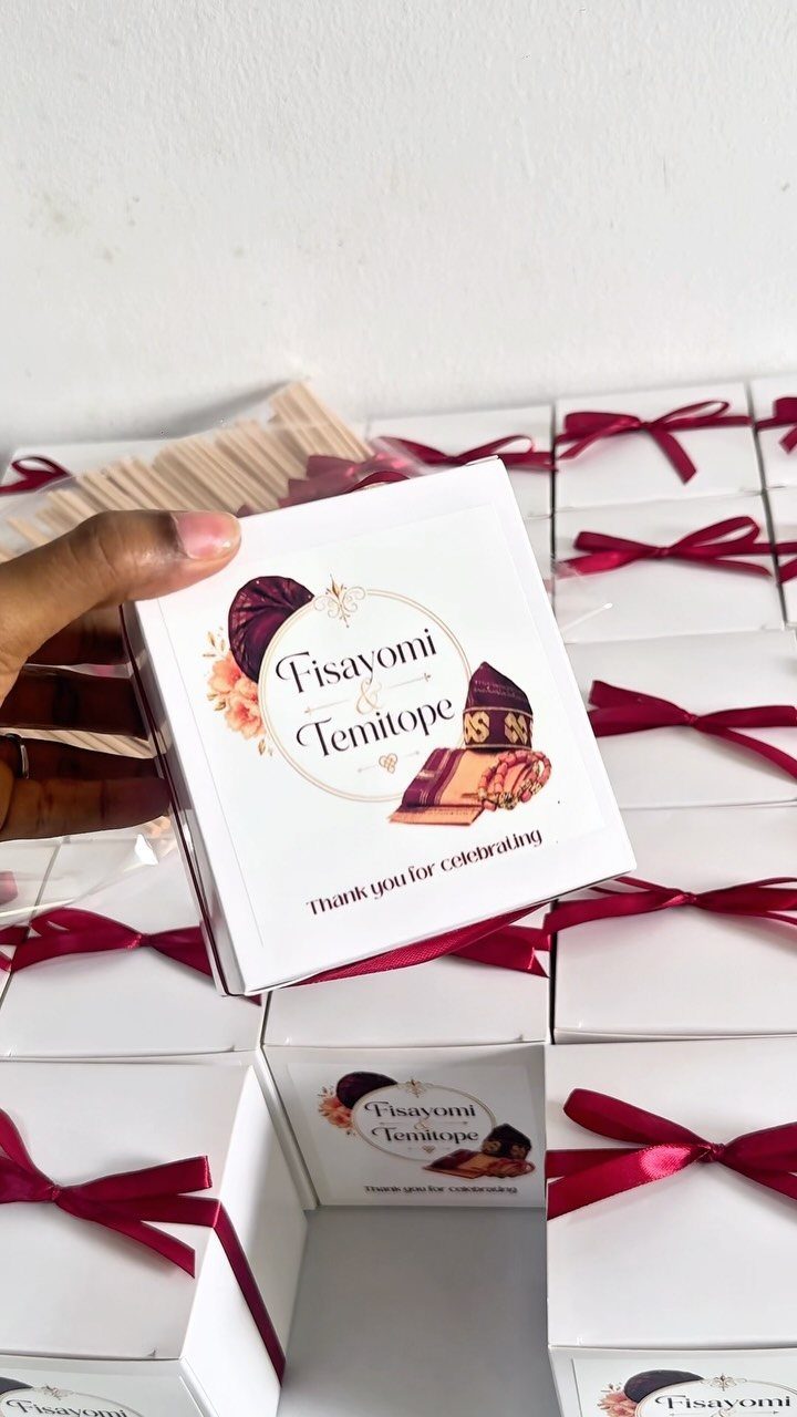 Hand holding a personalized white gift box among several ribbon-tied favor boxes.