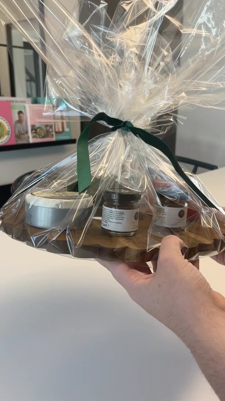 Wooden platter gift basket with food jars wrapped in clear cellophane and green ribbon