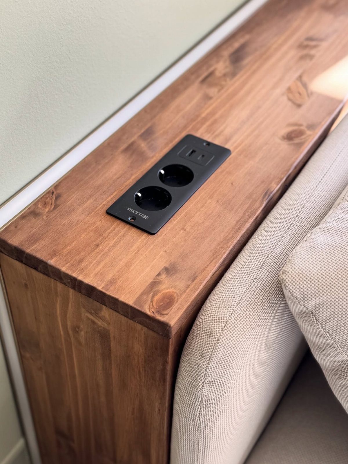 Black electrical outlet and USB ports built into a wooden surface by a sofa.
