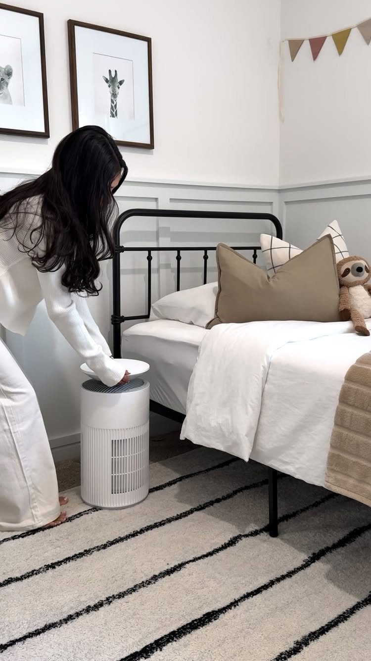 Woman placing a lid on a white air purifier next to a bed.
