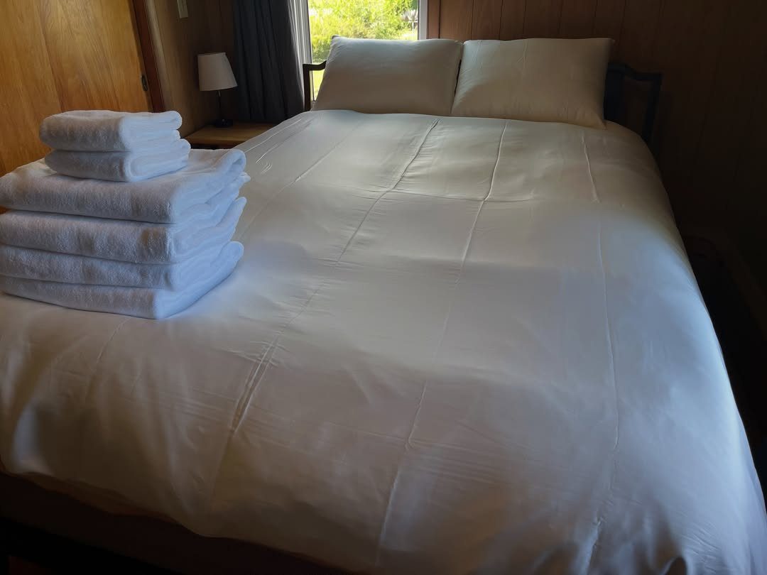 Stacked white towels on a neatly made bed with white linens and pillows.