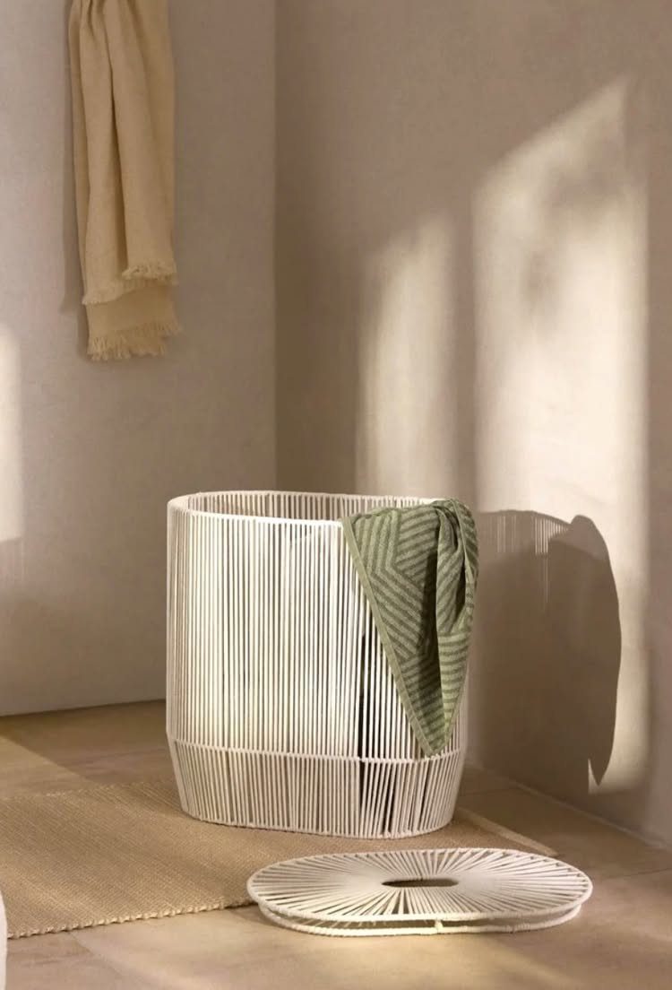White woven laundry basket with a green striped towel in a neutral room.