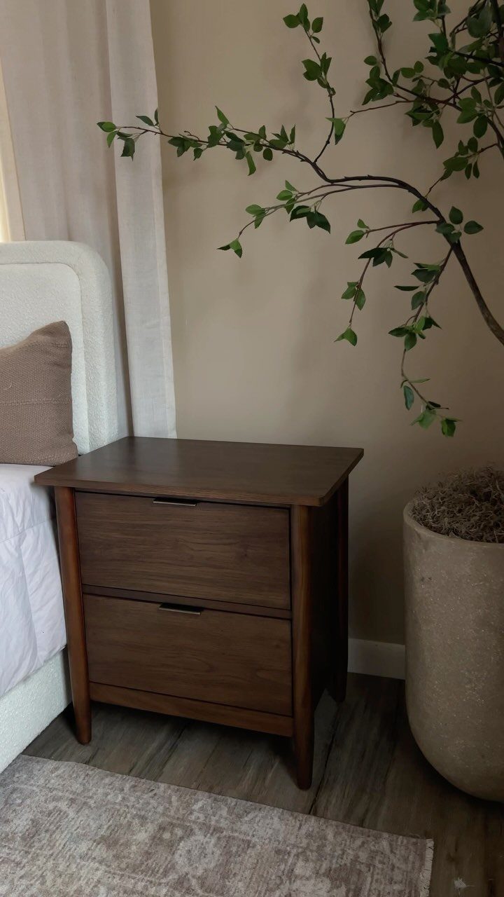 Dark brown wooden nightstand with two drawers next to a white bed.
