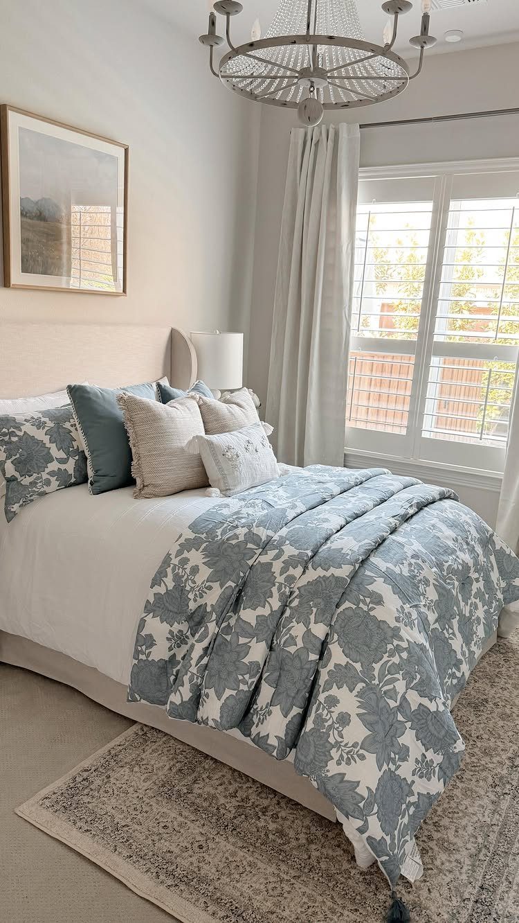Bed with blue floral duvet and decorative pillows in a bright guest room.