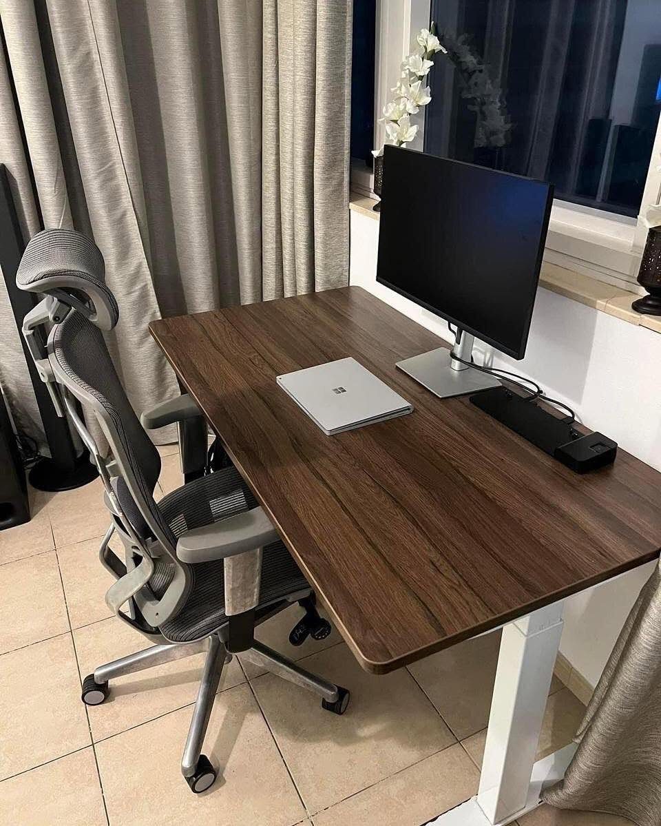 Grey ergonomic mesh office chair at a dark wood desk with a monitor.