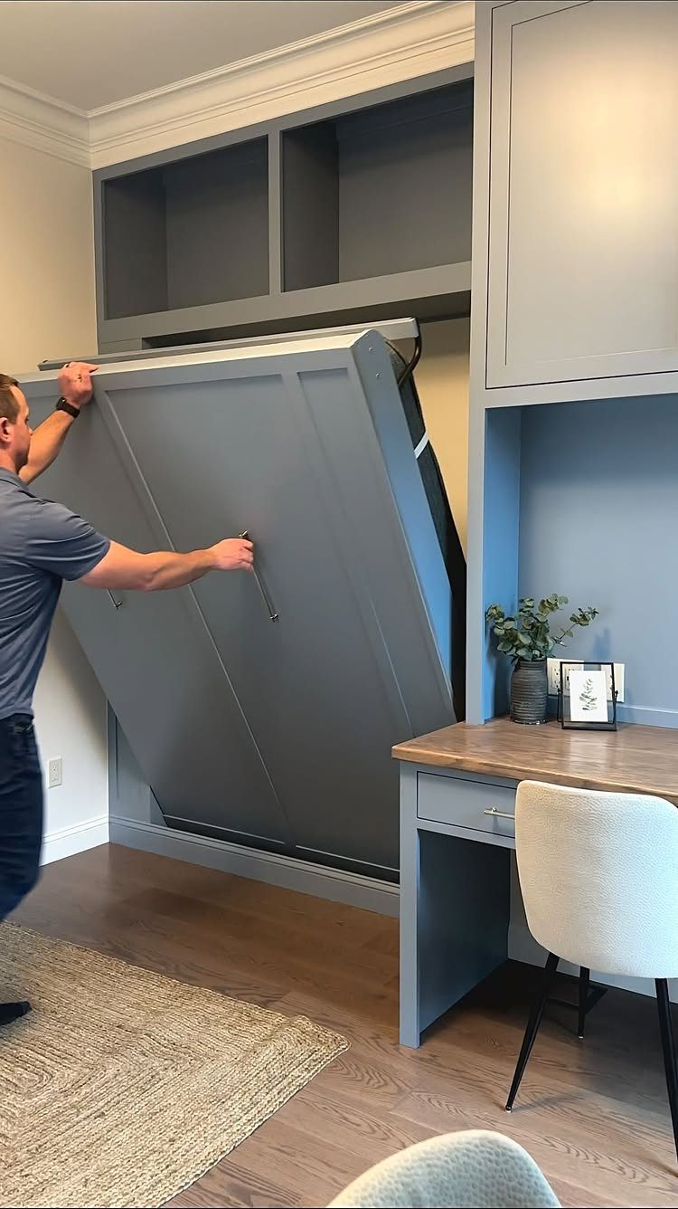 Man pulling down a grey Murphy bed in a combined office guest room.