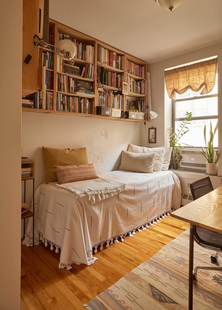 Small room with a single bed, wooden desk, and overhead built-in bookshelves.