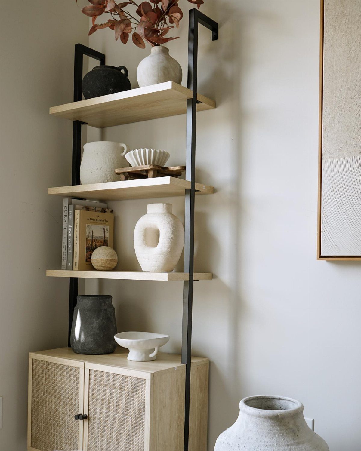 Tall shelving unit with light wood shelves and black metal frame holding ceramics.
