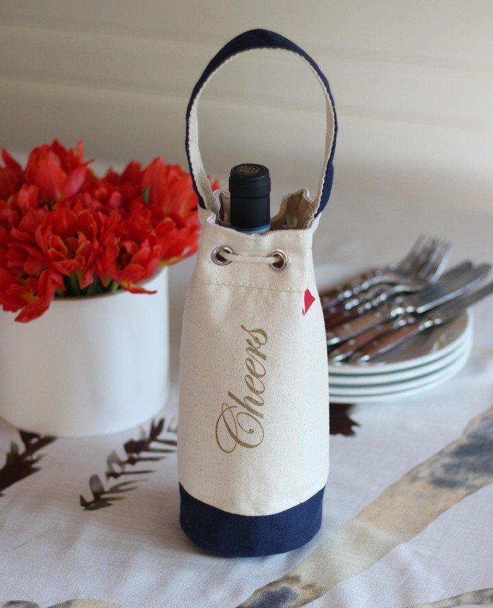 Wine bottle in a cream and blue fabric bag with Cheers written on it.
