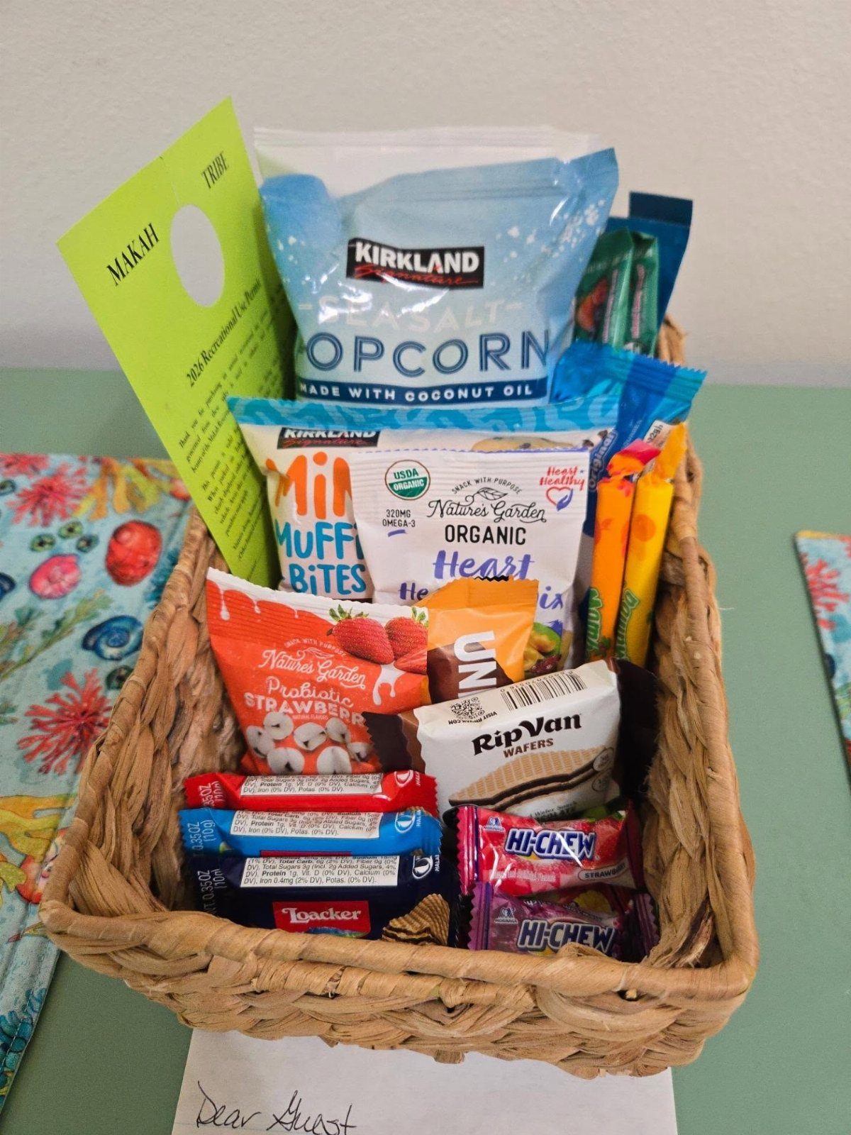 Woven wicker basket filled with assorted packaged snacks and a welcome note.