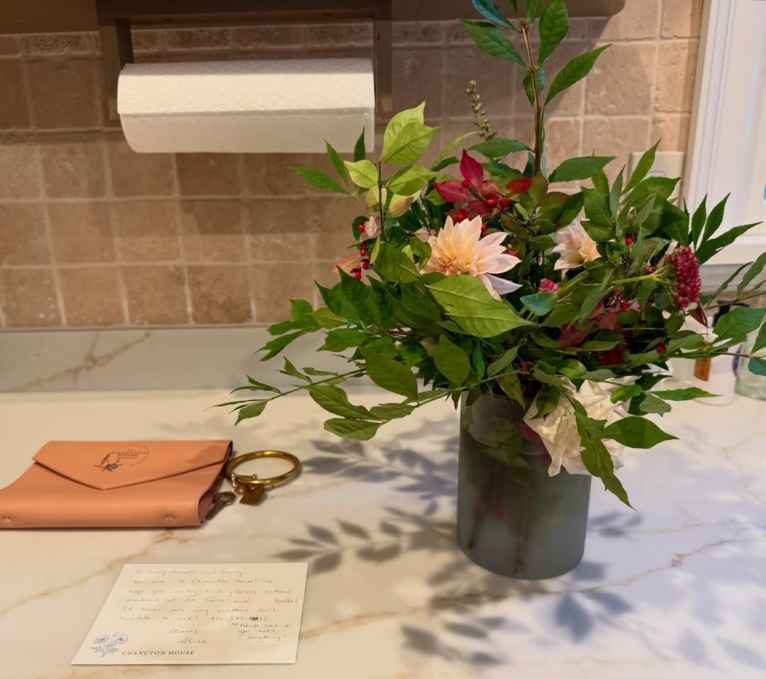 Handwritten note and peach envelope next to a floral arrangement on marble counter.