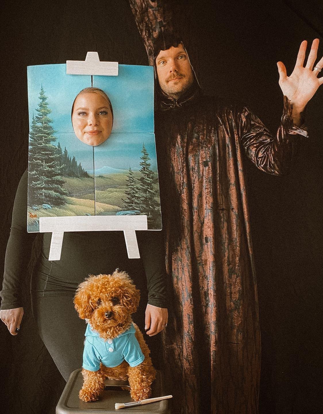 Man dressed as Bob Ross standing next to woman dressed as his painting.