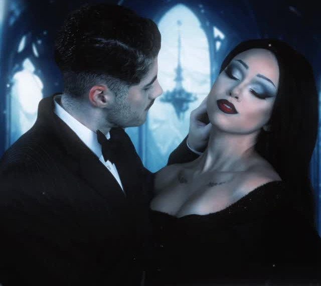 Couple dressed as Gomez and Morticia Addams posing in a gothic setting.