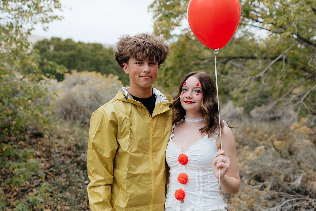 Teenage couple dressed as clowns, boy in yellow raincoat, girl with red balloon.