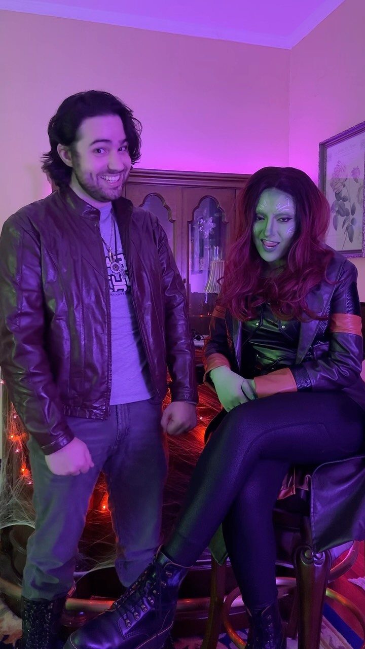 Man in brown leather jacket and woman with green skin in cosplay costumes.