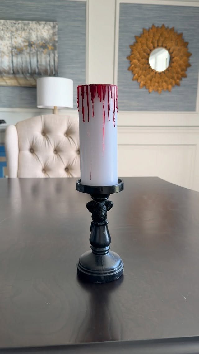 White pillar candle with red dripping wax on a black ornate holder.