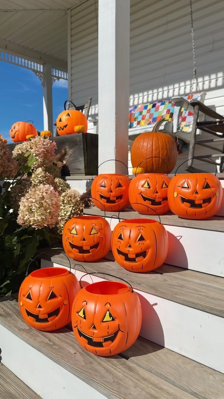 Plastic jack-o'-lantern buckets and a real pumpkin arranged on white porch steps.