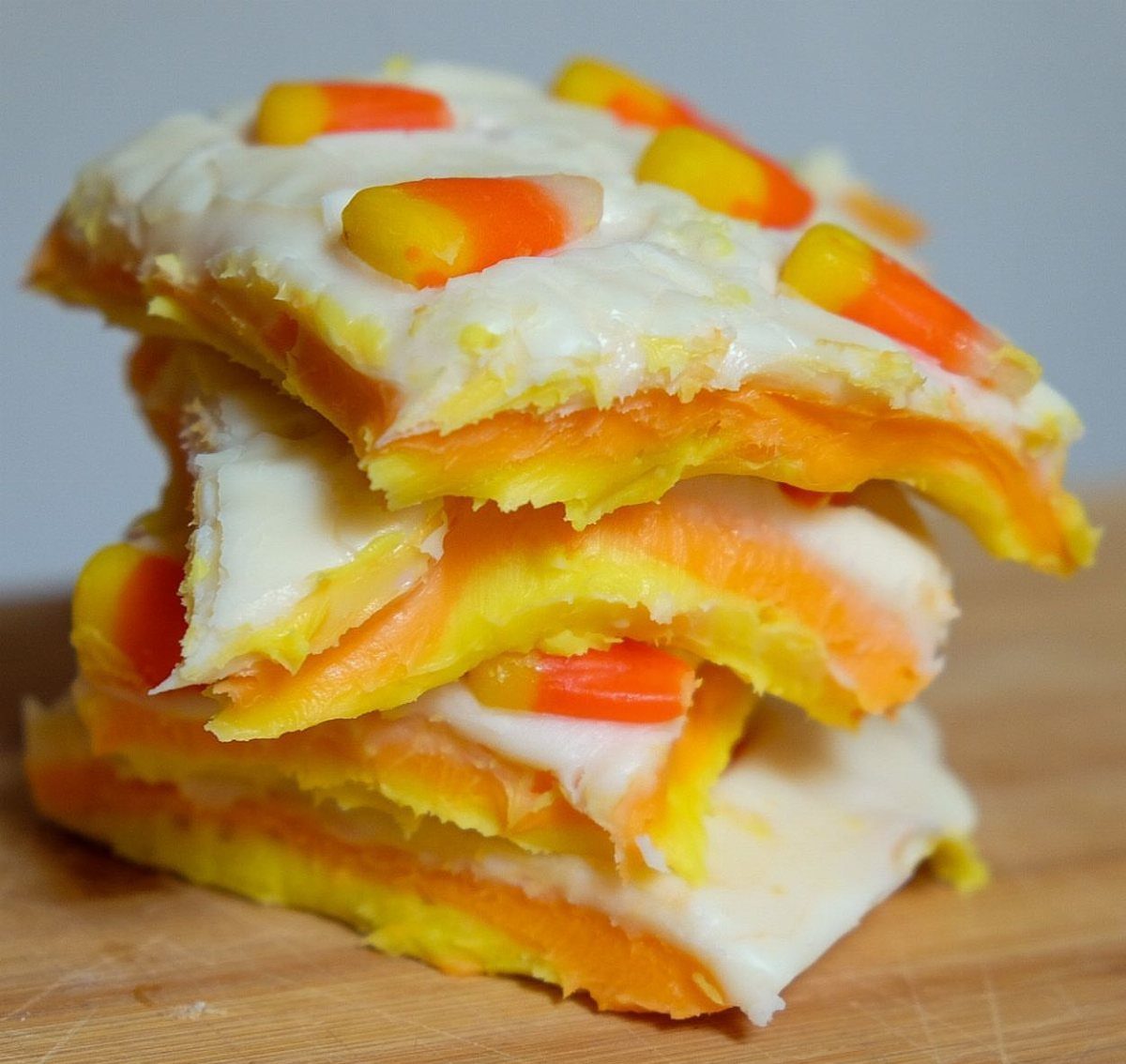 Layered white, orange, and yellow fudge topped with candy corn on wood.