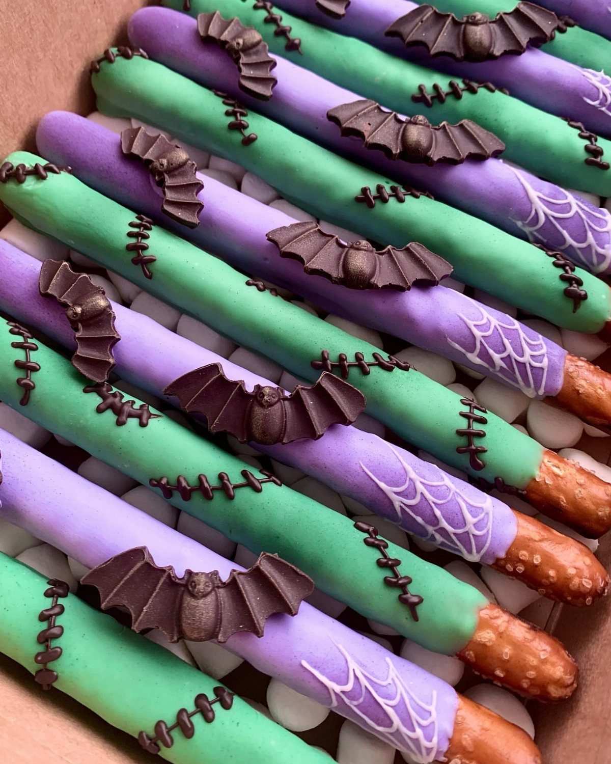Chocolate-covered pretzel rods in green and purple with bat and spider web decorations.