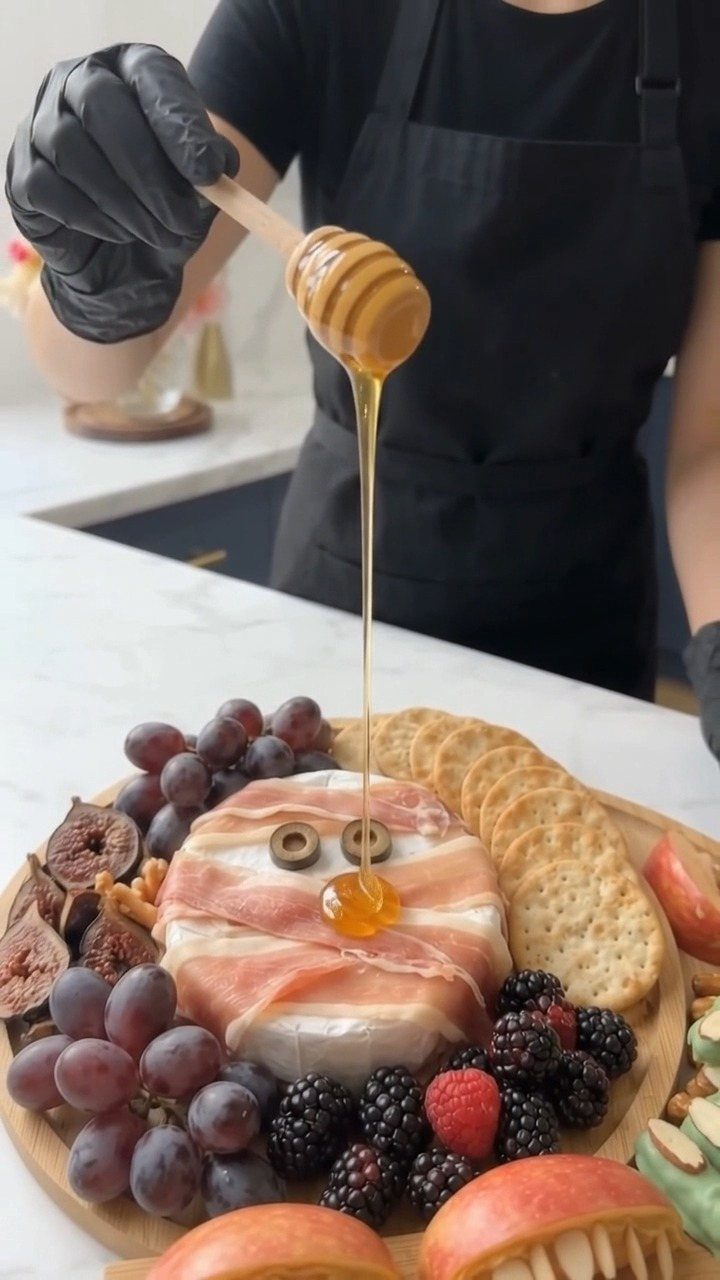 Charcuterie board with a prosciutto face made of cheese, olives, and honey.