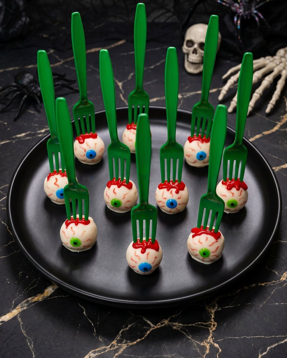 Eyeball appetizers on green forks arranged on a black plate with spooky decor.