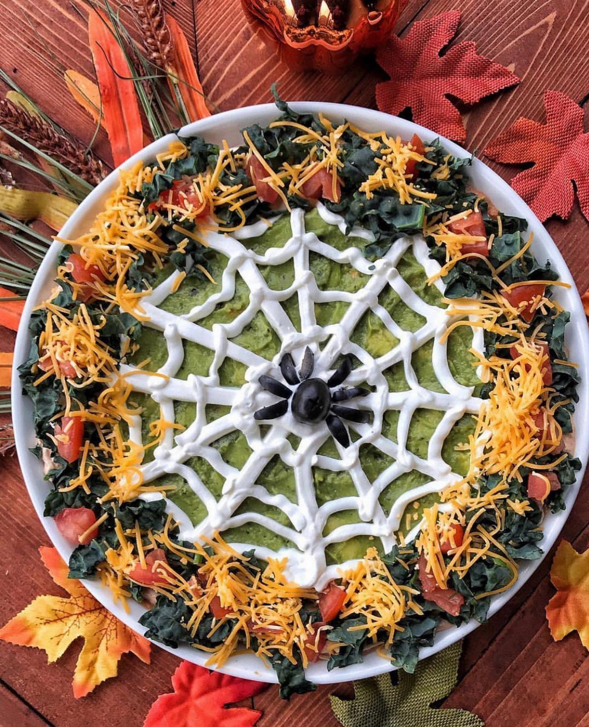 Layered taco dip with a sour cream spiderweb and olive spider on top.