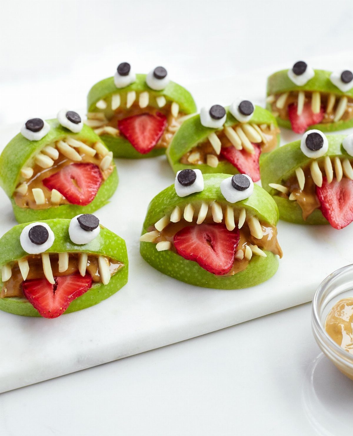 Monster apple bites with strawberry tongues and almond teeth on marble surface.