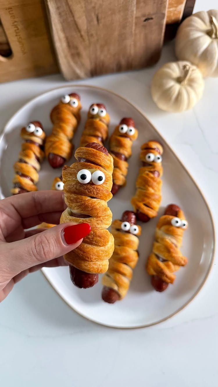Mummy dogs wrapped in pastry with candy eyes on a white platter.