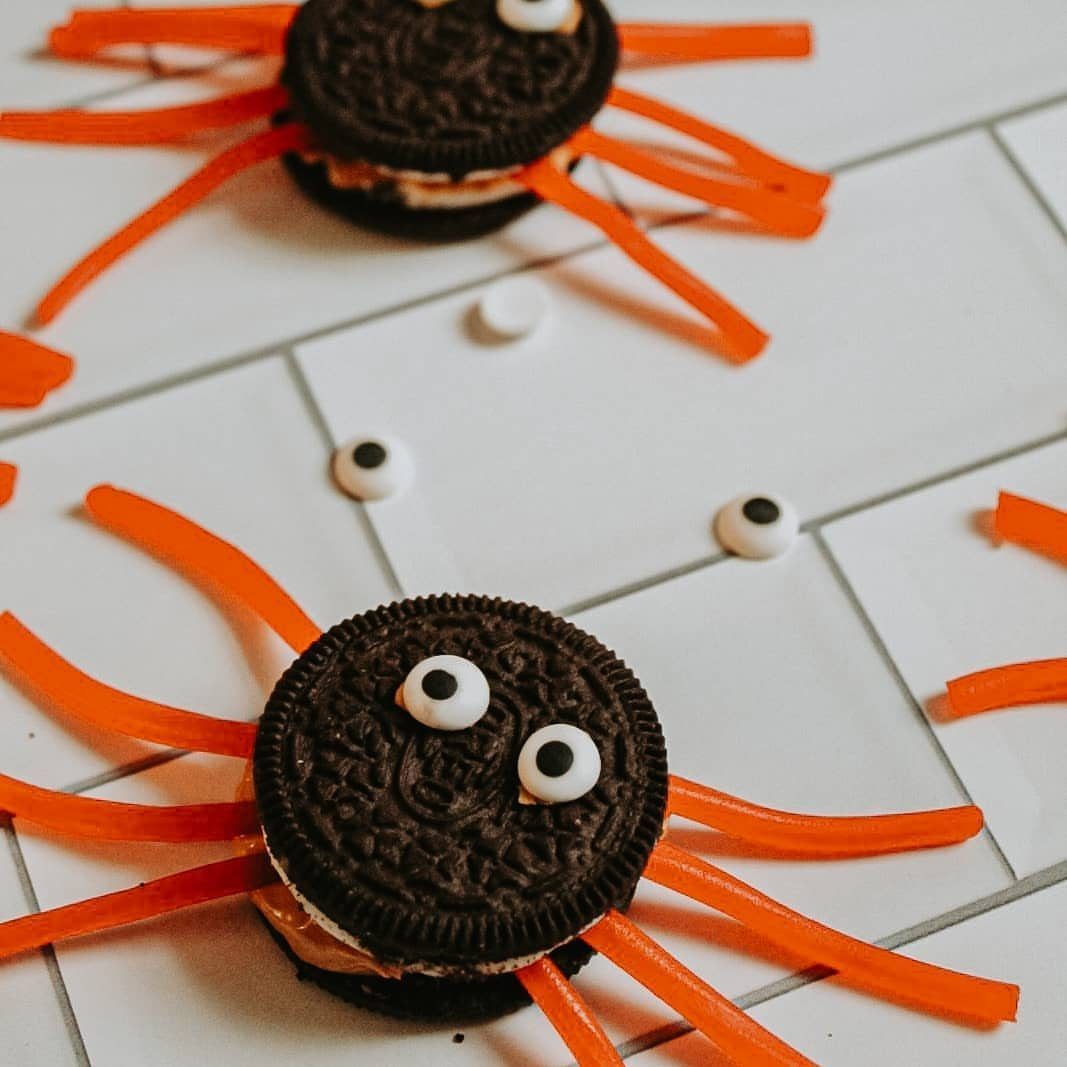 Chocolate sandwich cookies decorated as spiders with orange candy legs and candy eyes.