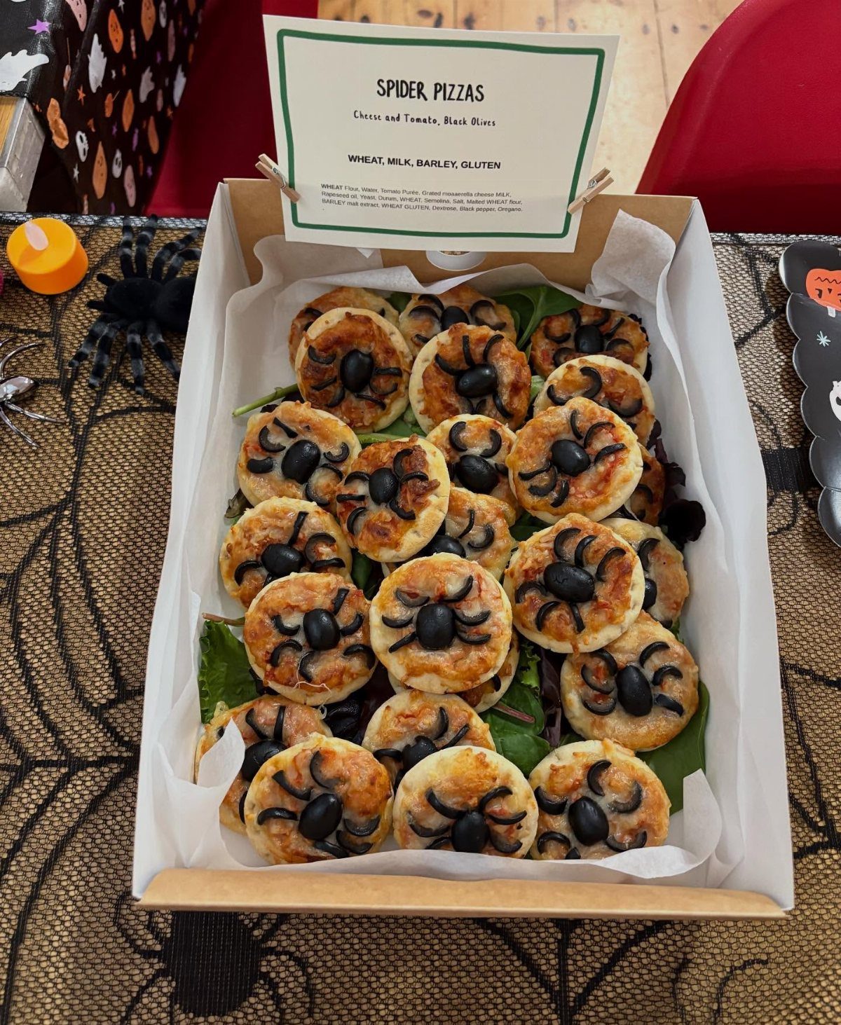 Spider mini pizzas with olive eyes and legs in a cardboard box.