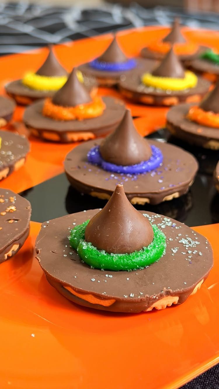 Witch hat cookies made with chocolate, colorful frosting, and chocolate kisses on orange plate