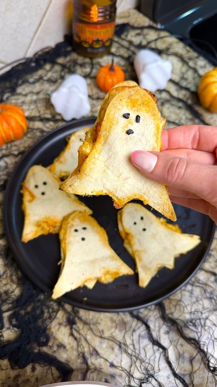 Ghost-shaped toasted cheese sandwiches on a black plate with Halloween decorations.