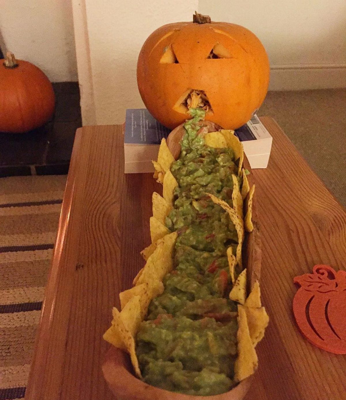 Carved pumpkin with guacamole flowing from its mouth onto a chip platter.