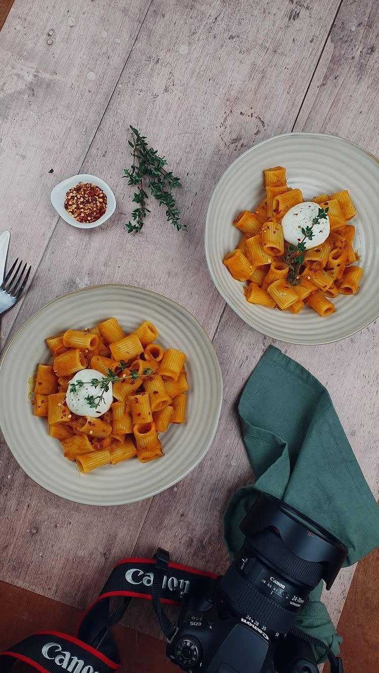 Orange pumpkin pasta in two bowls topped with white cheese on wooden table
