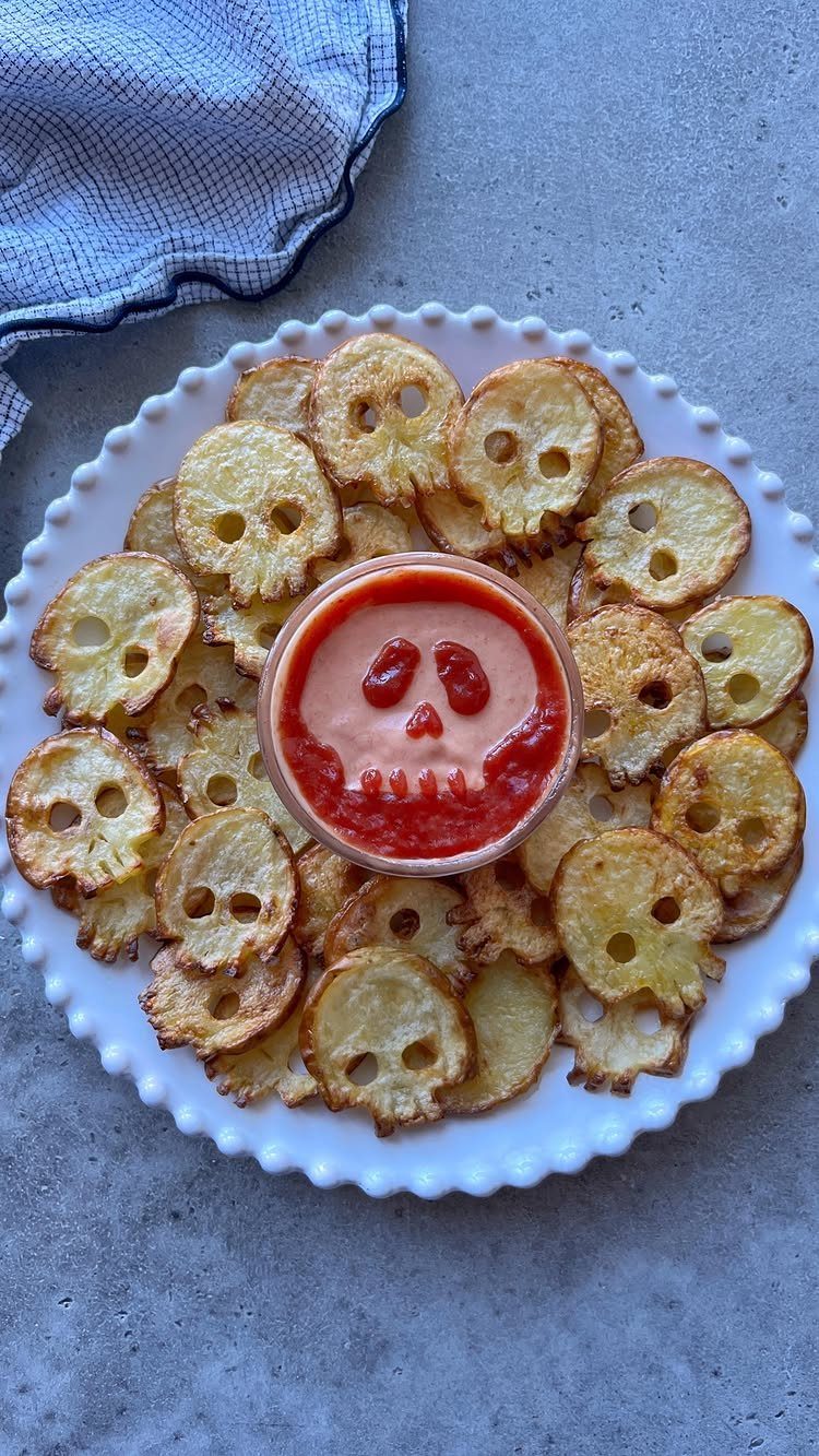 Skull-shaped potato slices on a white plate with a red dipping sauce bowl.
