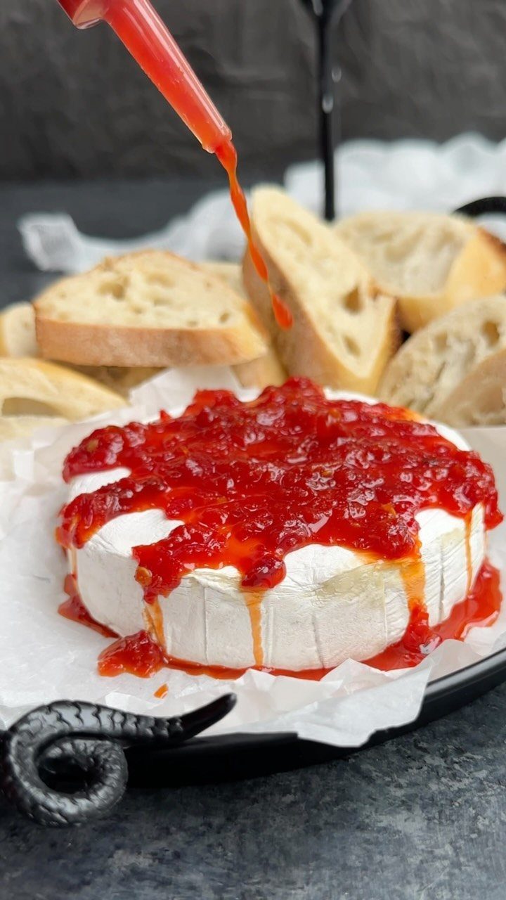 Baked brie cheese topped with dripping red jam served with sliced baguette bread