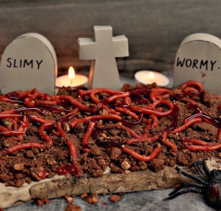 Red gummy worms on chocolate crumble with tombstones and candles for Halloween.