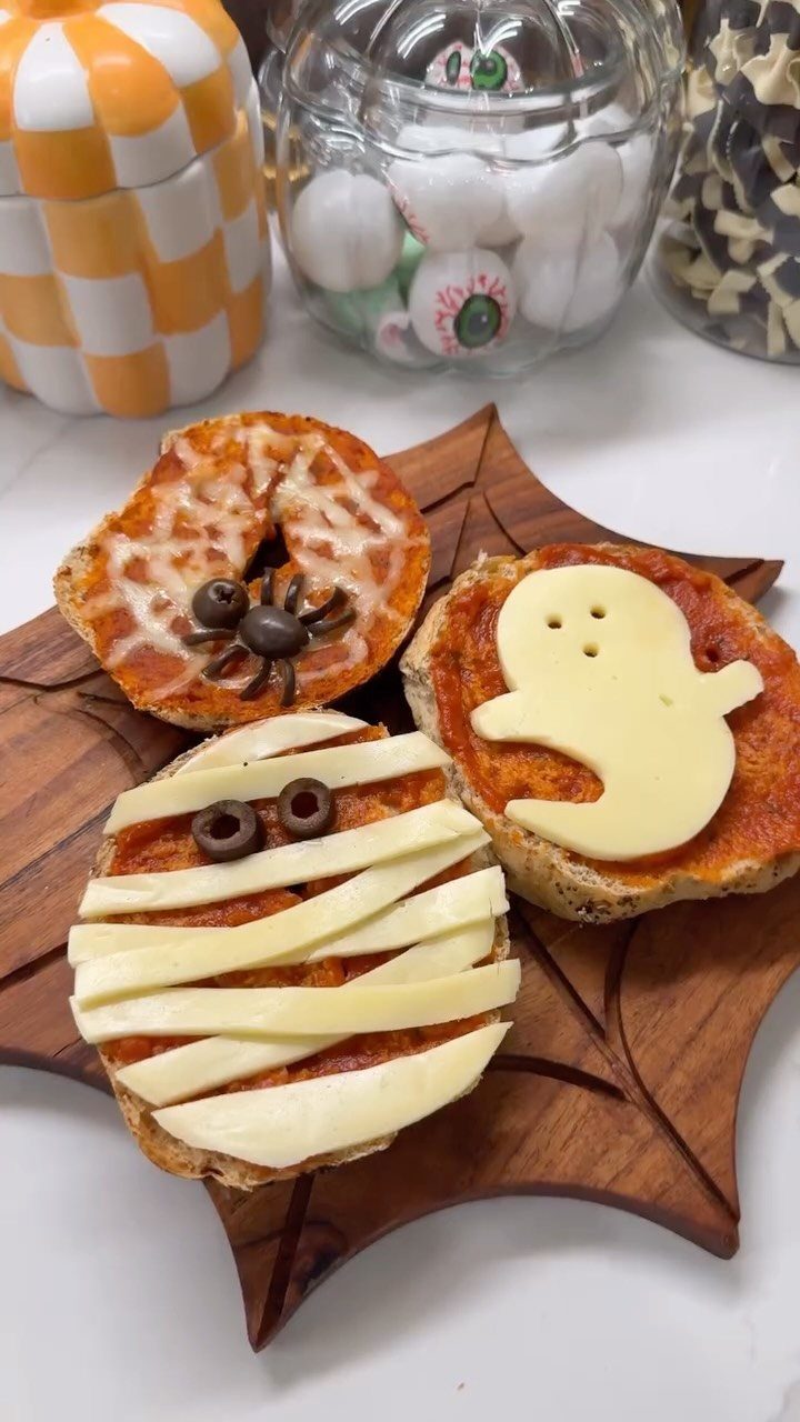 Mini pizza bagels decorated as a ghost, mummy, and spider on a platter